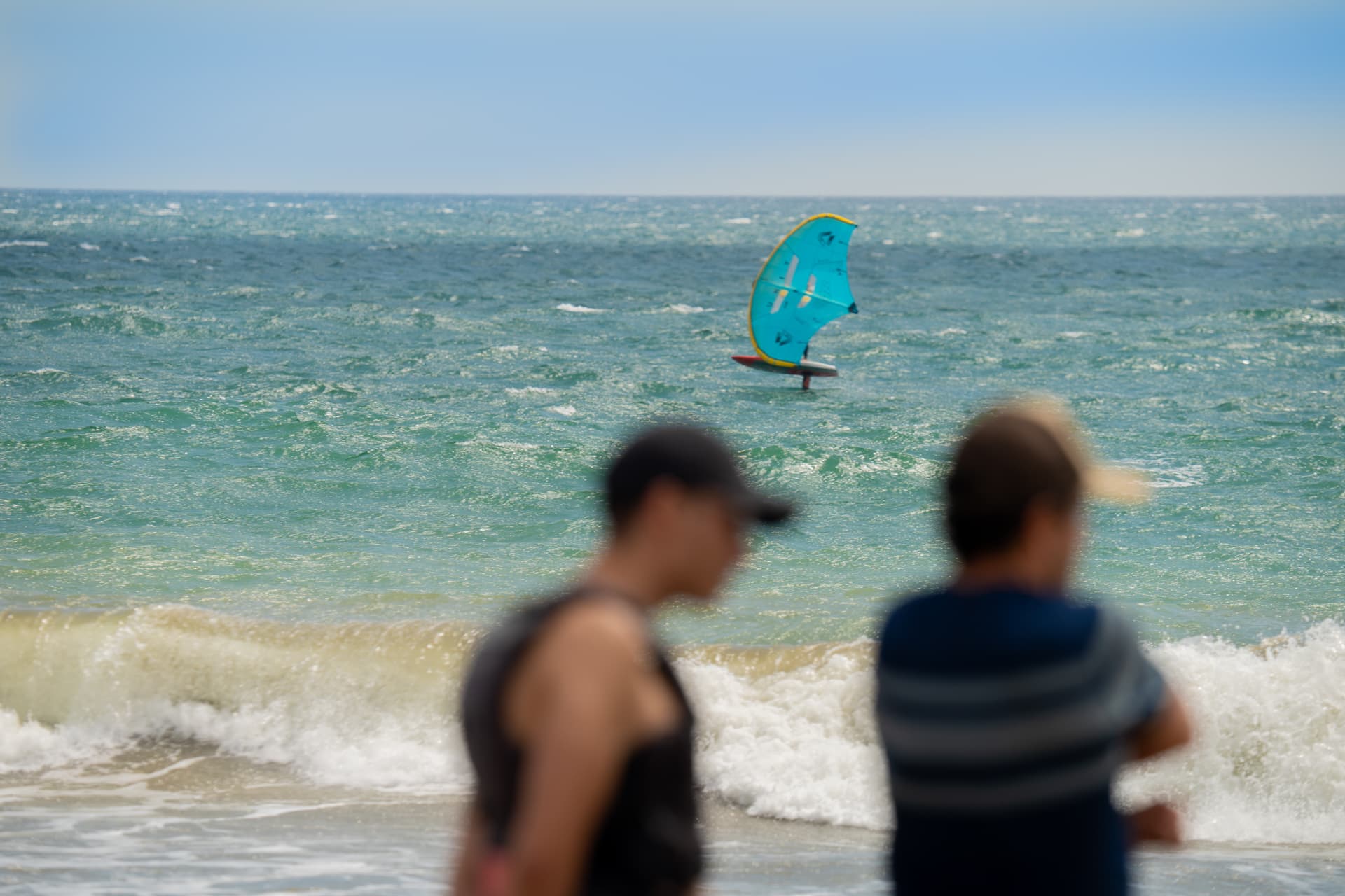 A young kitesurfer walking along the beach carrying her twin-tip board
