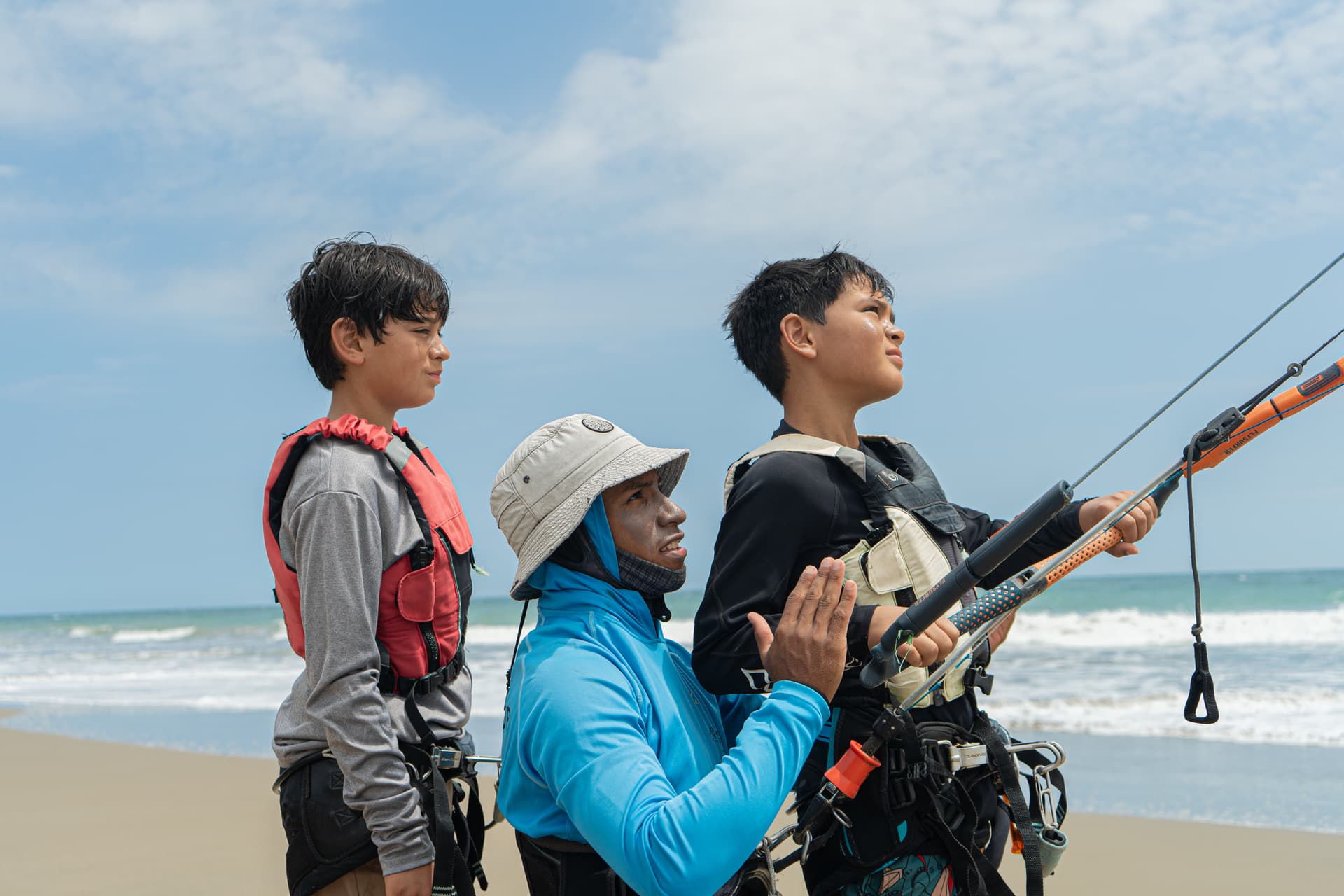 A kitesurf instructor teaching two teenagers how to handle the kite control bar on the beach